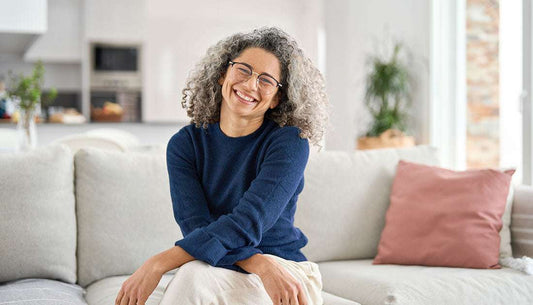 Smiling woman sitting on a sofa, representing tips to reduce menopause symptoms.