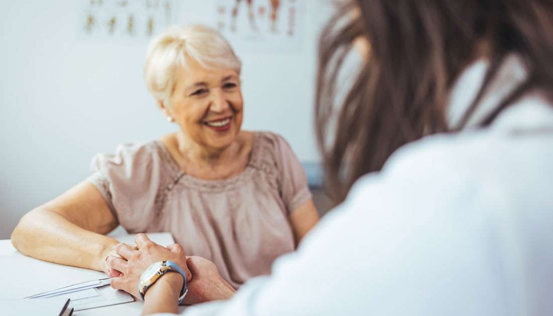 A smiling elderly woman discussing ways to prevent Parkinson's disease progression with a healthcare professional.